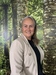 Bonnie Matehaere, a Māori woman, is smiling in front of a backdrop of New  Zealand native forest