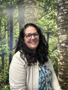 Cherie Seamark, a Māori woman, is smiling in front of a backdrop of New  Zealand native forest